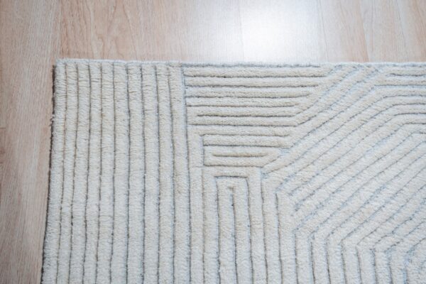 Textured cream rug featuring raised, parallel geometric stripes separated by recessed gray lines on wood flooring.