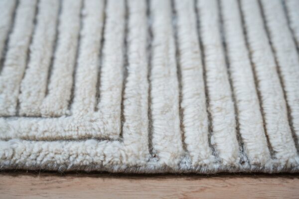 Extreme close-up shows a cream high-pile rug with deeply carved vertical lines and a geometric corner on a wood floor.