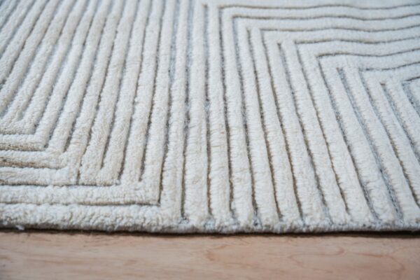 Cream textured rug with raised ridges forming angular geometric patterns on wood flooring.