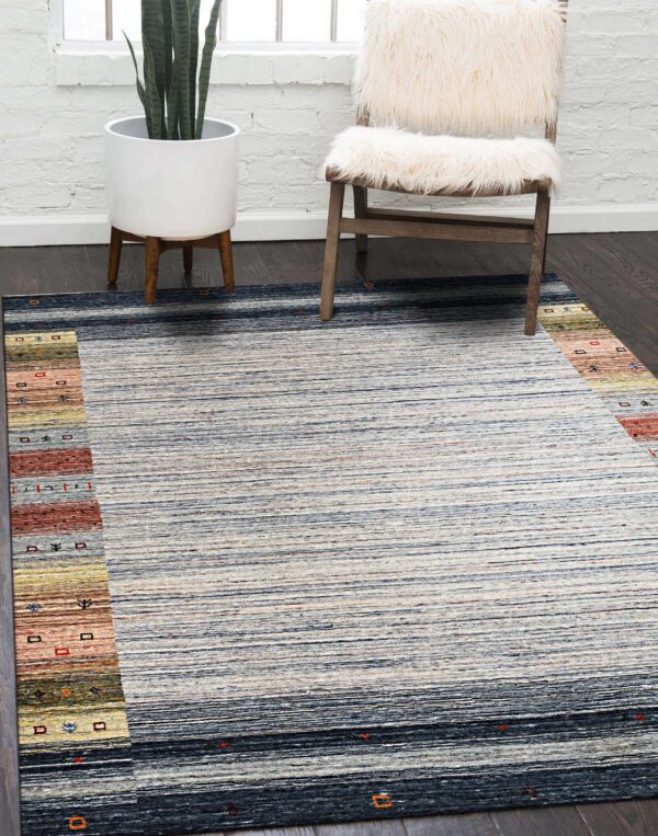 Striped blue and cream rug with multicolored borders on dark wood, next to a white furry chair.