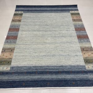 Variegated blue rug with a wide striped border displaying earth tones and small geometric motifs on white tile.