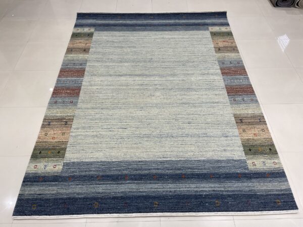 Variegated blue rug with a wide striped border displaying earth tones and small geometric motifs on white tile.