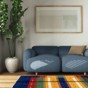 Sunlight casts striped shadows across a blue sofa and a vibrant multicolored striped rug on wood flooring.