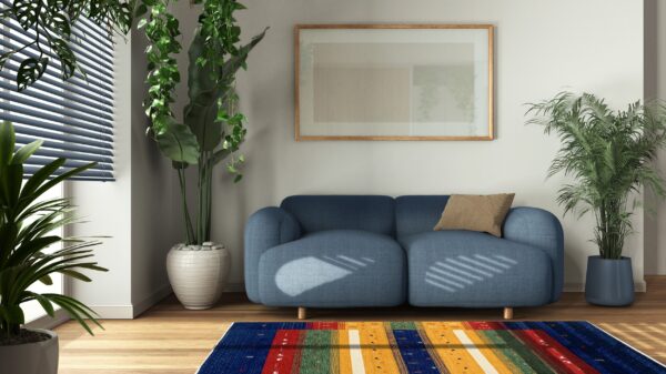 Sunlight casts striped shadows across a blue sofa and a vibrant multicolored striped rug on wood flooring.