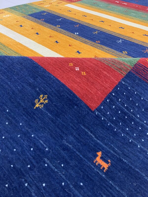 Colorful folded rug displays multi-colored stripes and contrasting red and blue geometric patterns.