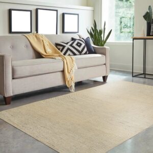 Light tan geometric low-pile rug placed under a tufted sofa on a gray concrete floor near a large window.