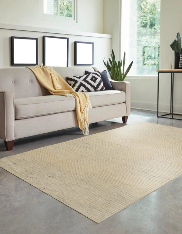 Light tan geometric low-pile rug placed under a tufted sofa on a gray concrete floor near a large window.