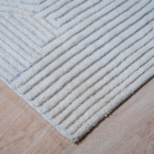 High-pile ivory rug corner displaying defined textured ridges over light wood plank flooring.