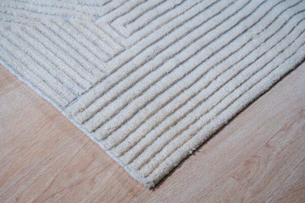 High-pile ivory rug corner displaying defined textured ridges over light wood plank flooring.