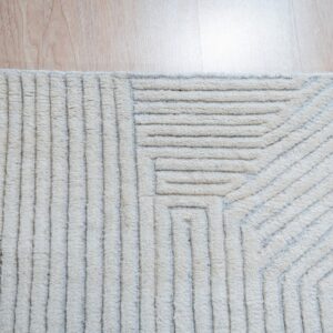 Close-up of a cream rug featuring raised, geometric, high-low texture on light wood planks.