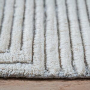 Cream-colored high-pile rug with pronounced vertical ridges and a zig-zag texture resting on wood.