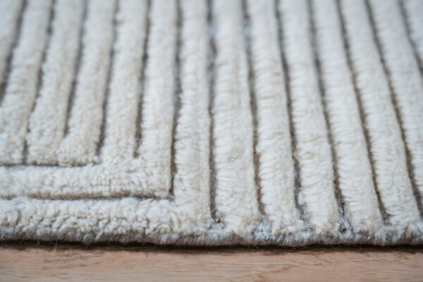 Cream-colored high-pile rug with pronounced vertical ridges and a zig-zag texture resting on wood.