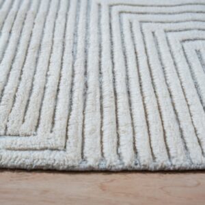 Cream, high-pile rug with deep, ridged stripes forming a recursive geometric pattern on wood.