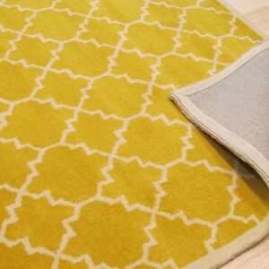 Close-up of a yellow geometric rug flipped to show the gray woven backing on light wood flooring.