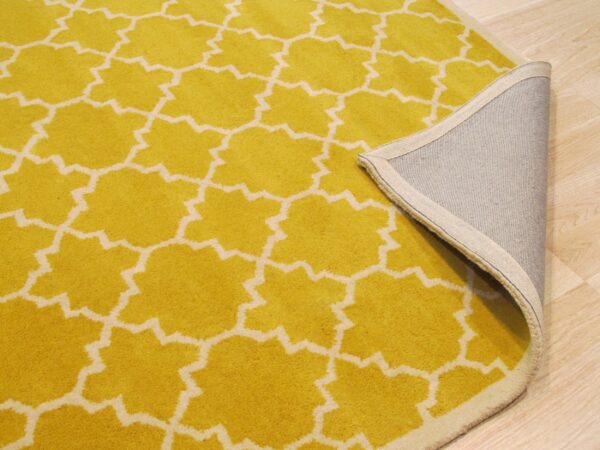 Close-up of a yellow geometric rug flipped to show the gray woven backing on light wood flooring.