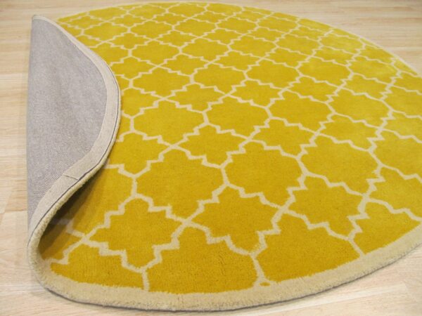 Yellow and cream round rug with a trellis pattern folded back to show the gray backing on wood floor.
