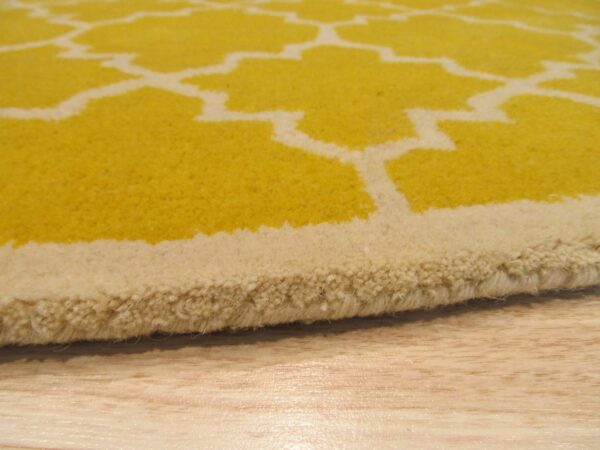 Close-up shows a thick yellow rug with a cream geometric pattern resting on light wood flooring.