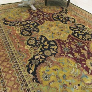Traditional rug with gold, burgundy, and black floral designs bordered by rust tones on a light floor.