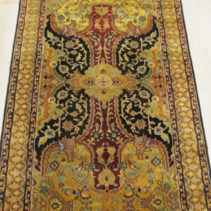 Ornate rectangular rug featuring black, yellow, and burgundy floral motifs on pale wooden plank flooring.