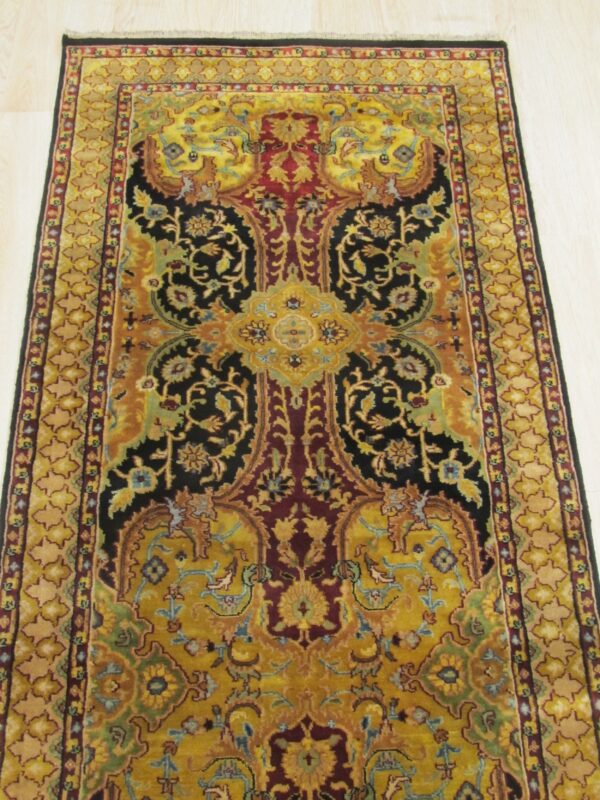 Ornate rectangular rug featuring black, yellow, and burgundy floral motifs on pale wooden plank flooring.