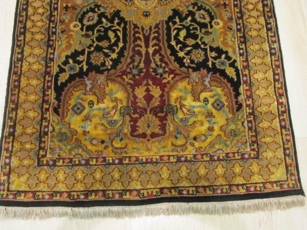 Gold, black, and red traditional rug with intricate floral patterns and a visible white fringe on light wood.