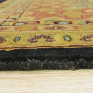 The black, high-pile edge of a gold and rust patterned rug sits on light wood planks.