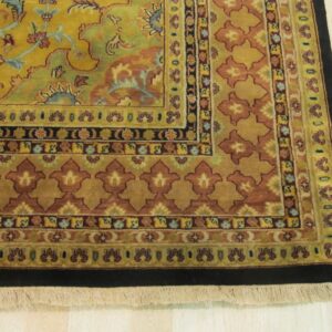 Gold, rust, and green traditional rug border with fringe and intricate patterns shown on light wood flooring.