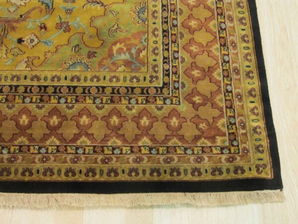 Gold, rust, and green traditional rug border with fringe and intricate patterns shown on light wood flooring.