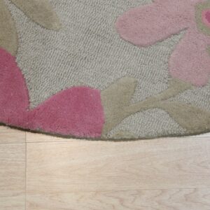Beige low-pile rug with raised pink and tan floral elements rests on light wood-look planks.