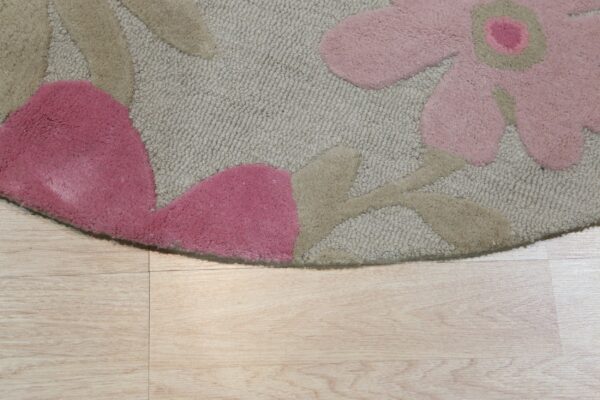 Beige low-pile rug with raised pink and tan floral elements rests on light wood-look planks.