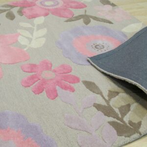 Floral rug in pink, lavender, and taupe with a gray fabric backing folded over light wood flooring.