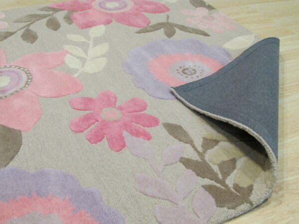 Floral rug in pink, lavender, and taupe with a gray fabric backing folded over light wood flooring.