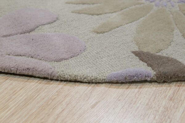 The carved floral rug features varying pile heights in beige, mauve, and brown on wood flooring.