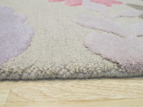 Thick beige pile rug featuring carved pink and purple abstract floral shapes rests on light wood flooring.