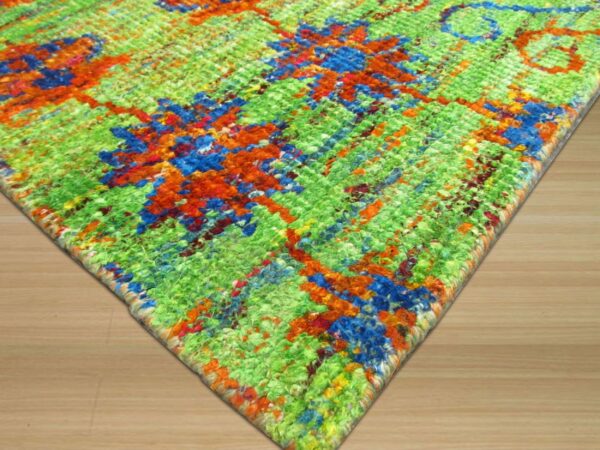 Vibrant, textured rug corner featuring green, blue, and orange abstract patterns on light wood flooring.