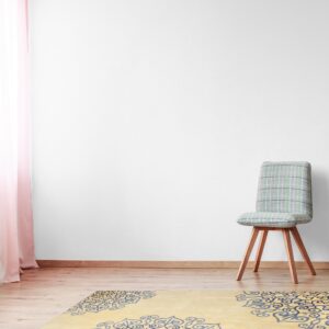 A light yellow rug with large blue and black medallion patterns is placed on a wood floor next to a checked chair.