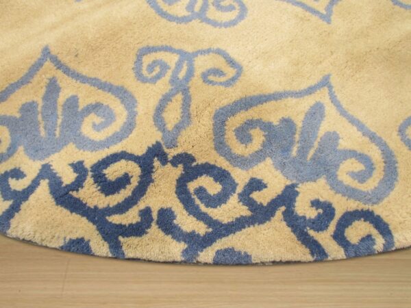Medium-pile tan rug featuring large, swirling light and dark blue patterns on wood flooring.