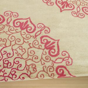 A beige medium-pile rug with pink scrollwork and heart-shaped motifs rests on light wood flooring.