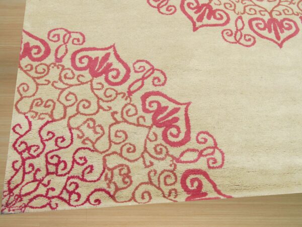 A beige medium-pile rug with pink scrollwork and heart-shaped motifs rests on light wood flooring.