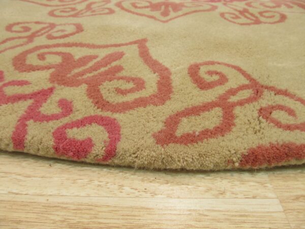 Textured close-up of a beige, medium-pile rug patterned with bold pink scrollwork on light wood floor.