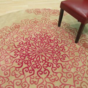 Round beige rug with a pink medallion pattern on wood floor, partially covered by a red chair.