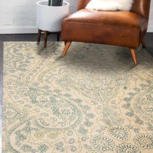 Beige rug with teal and olive green paisley patterns under a brown leather chair and houseplant.