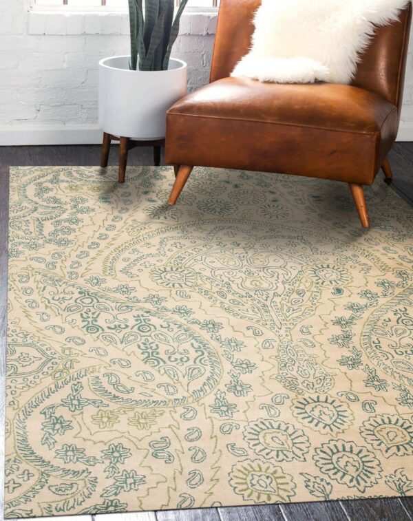Beige rug with teal and olive green paisley patterns under a brown leather chair and houseplant.