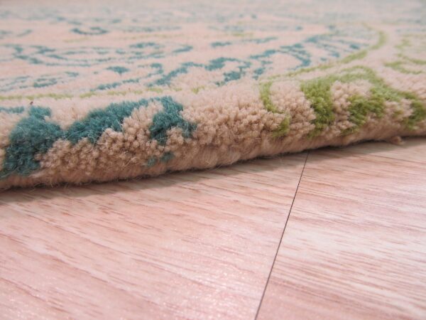 High-pile rug in beige, teal, and green with a stylized pattern lies on light wood flooring.