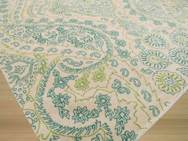 Cream textured rug with a bright teal and lime green paisley and floral pattern on wood floor.