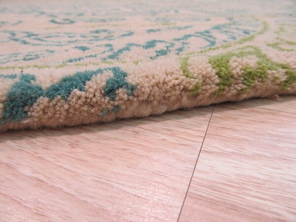 Medium-pile rug detail showing beige, teal, and green pattern on a light wood floor.