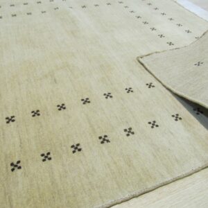 Light beige rug with scattered dark geometric patterns lies on wood flooring, revealing the backing.