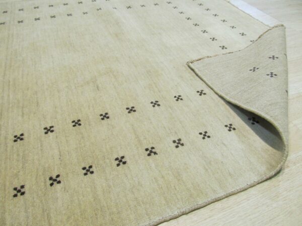 Light beige rug with scattered dark geometric patterns lies on wood flooring, revealing the backing.