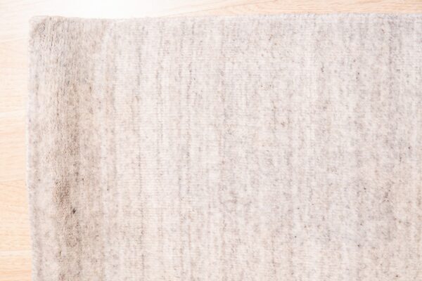 Speckled light beige rug with a textured surface lying on a bright wooden floor.