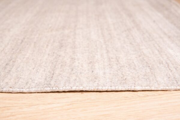 Close-up of a tightly bound light oatmeal rug resting on bright wood plank flooring.
